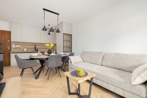 Una sala de estar moderna con un sofá gris, una mesa de comedor con sillas y una zona de cocina con armarios y una encimera de madera.