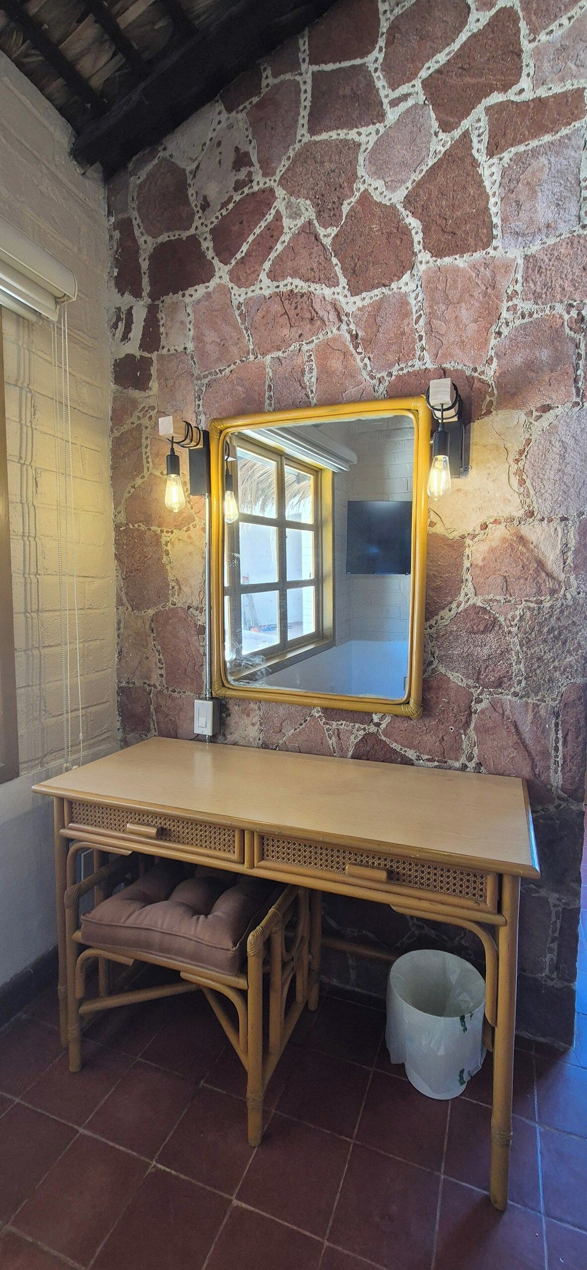 A room with a stone wall, a wooden vanity with a mirror, and a window.