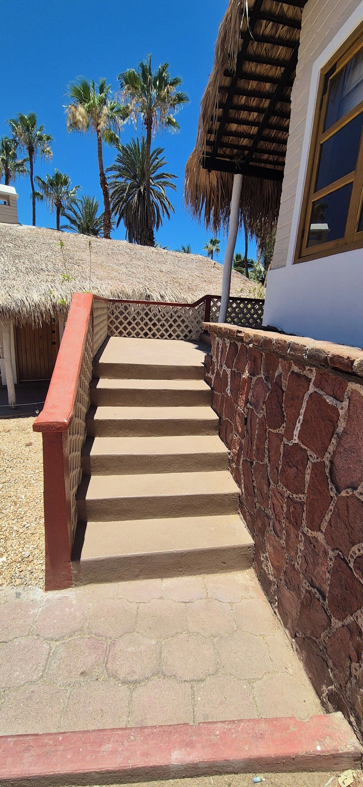A staircase leading to a building with a thatched roof, surrounded by palm trees.
