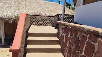 A staircase leading to a building with a thatched roof, surrounded by palm trees.
