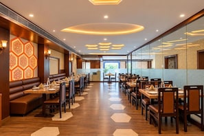 Un restaurant aux murs ornés de motifs hexagonaux, doté de planchers en bois et d’une allée centrale menant à un espace offrant une vue sur la verdure.