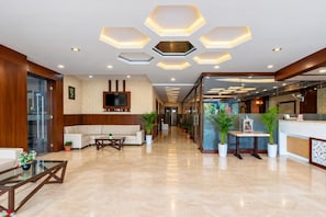Un hall d’hôtel comprenant un comptoir d’accueil, un espace salon et un design moderne au niveau du plafond.