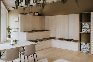 Ein modernes Interieur mit einem weißen Tisch, zwei Stühlen, einer Bank mit Kissen und einem Holzregal mit verzierten Boxen.