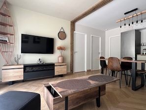 En moderne stue med et fladskærms-tv, møbler i træ og et spiseområde med stole og et bord.