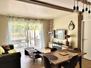 En moderne stue med sofa, spisebord, stole, fjernsyn og en skydedør, der fører til et udendørs område.