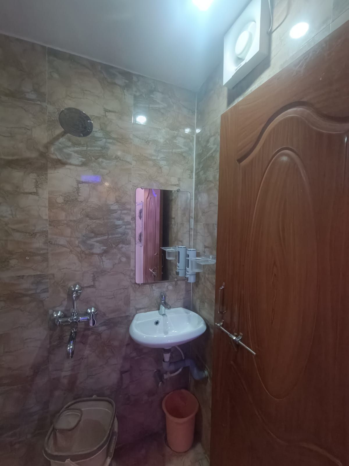 Ein Badezimmer mit Marmorwand, Waschbecken, Spiegel, Dusche und Holztür.