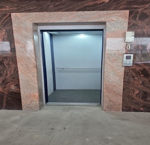 Een lift met een metalen binnenkant, een bedieningspaneel aan de muur en een marmeren wand eromheen.
