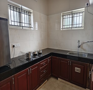 Una cocina con cubierta negra, armarios de madera, un lavamanos y dos ventanas con barrotes.