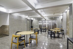 Un interior moderno con varias mesas y sillas, un techo alto con vigas a la vista y ventanas grandes.