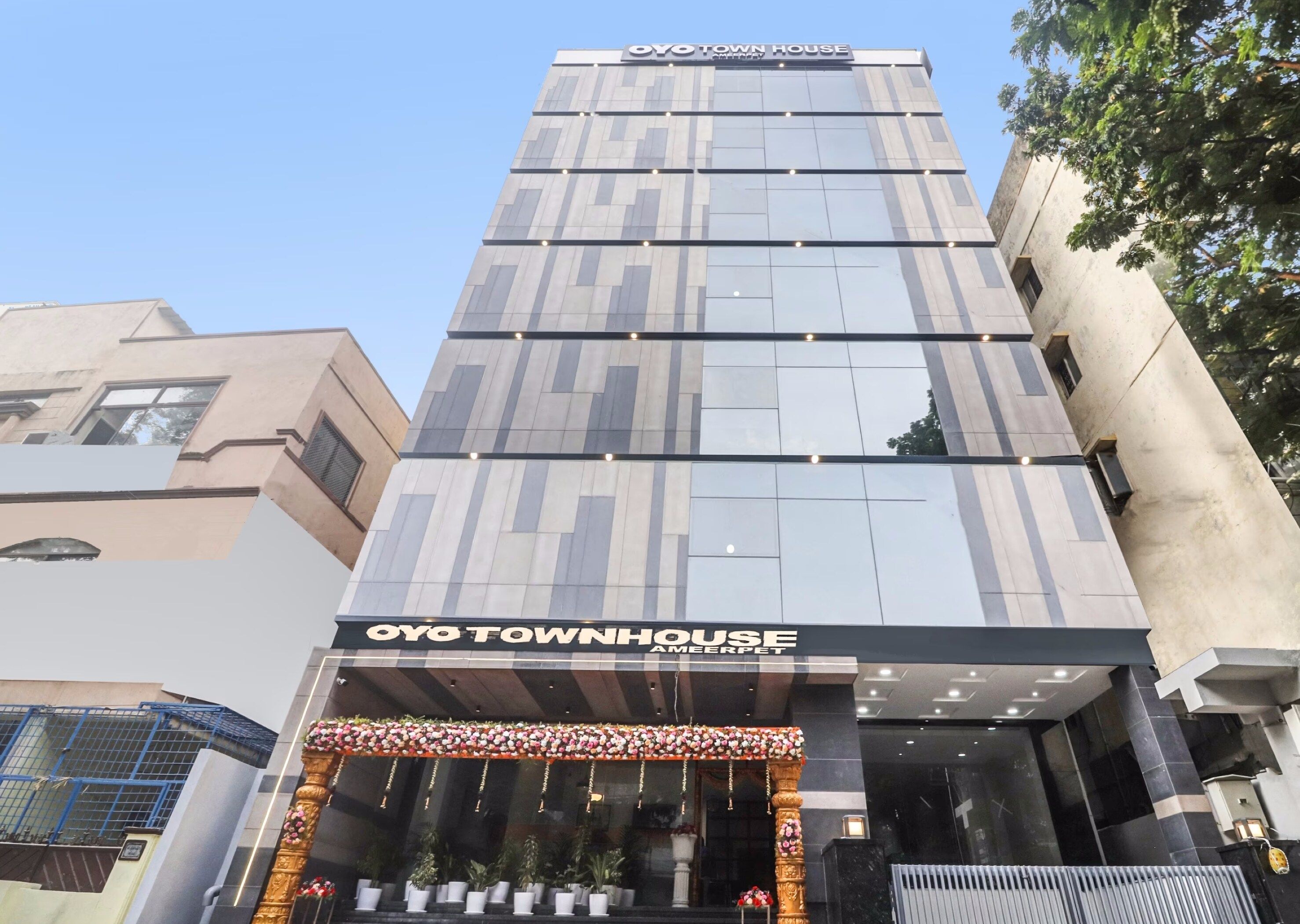 Un edificio de varios pisos con una fachada moderna, una entrada destacada con un arco decorativo y el nombre 'Oyo Townhouse' exhibido sobre la entrada.
