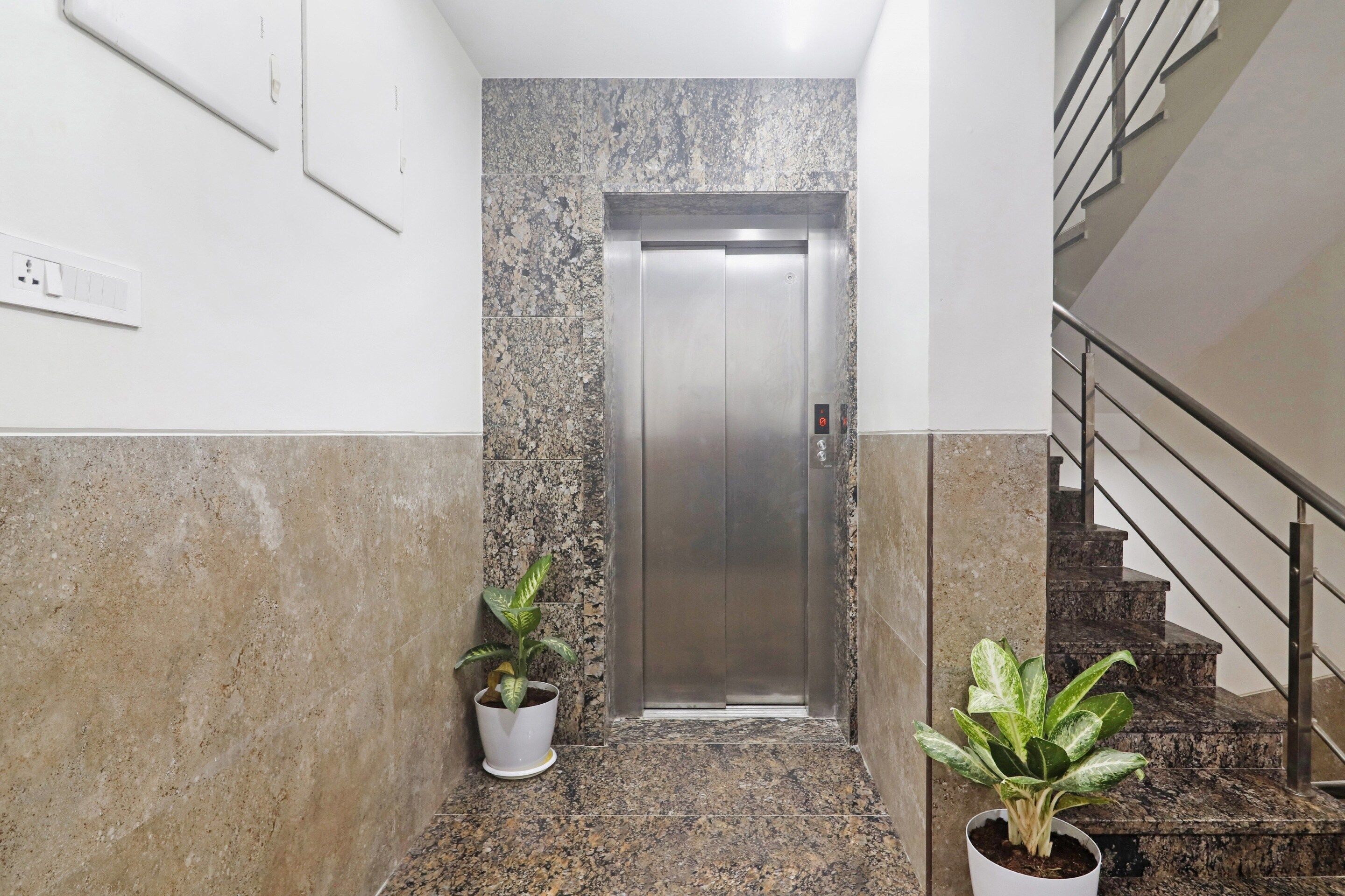 Un pasillo con piso de mármol, una puerta y dos plantas en macetas.