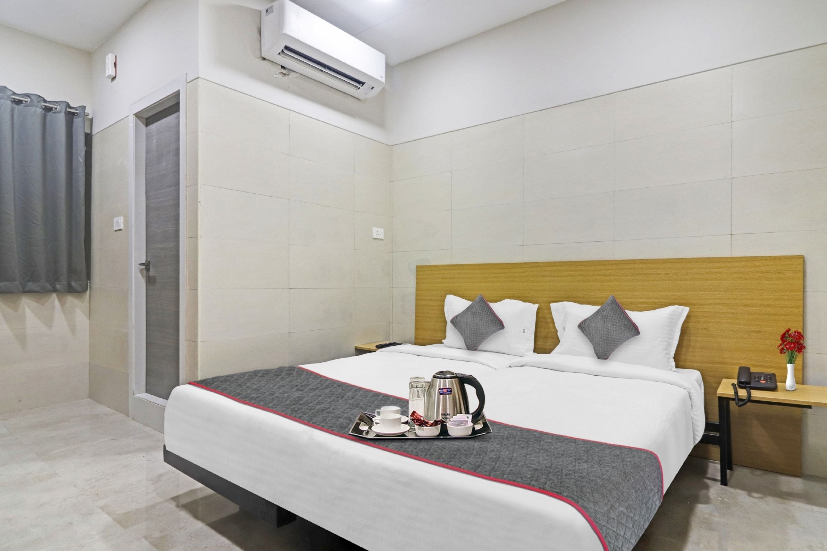 Habitación de hotel con cama, mesita de noche con teléfono y florero, unidad de aire acondicionado y zona de ducha.