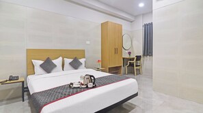 Habitación de hotel con cama, mesita de noche, armario de madera, escritorio con silla y espejo.