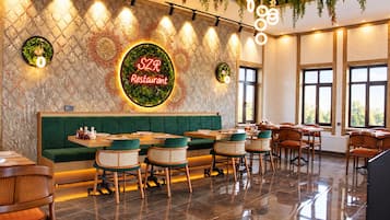 Interior de restaurante con área de asientos en cabina verde, mesas de madera, sillas de mimbre y un letrero de neón.