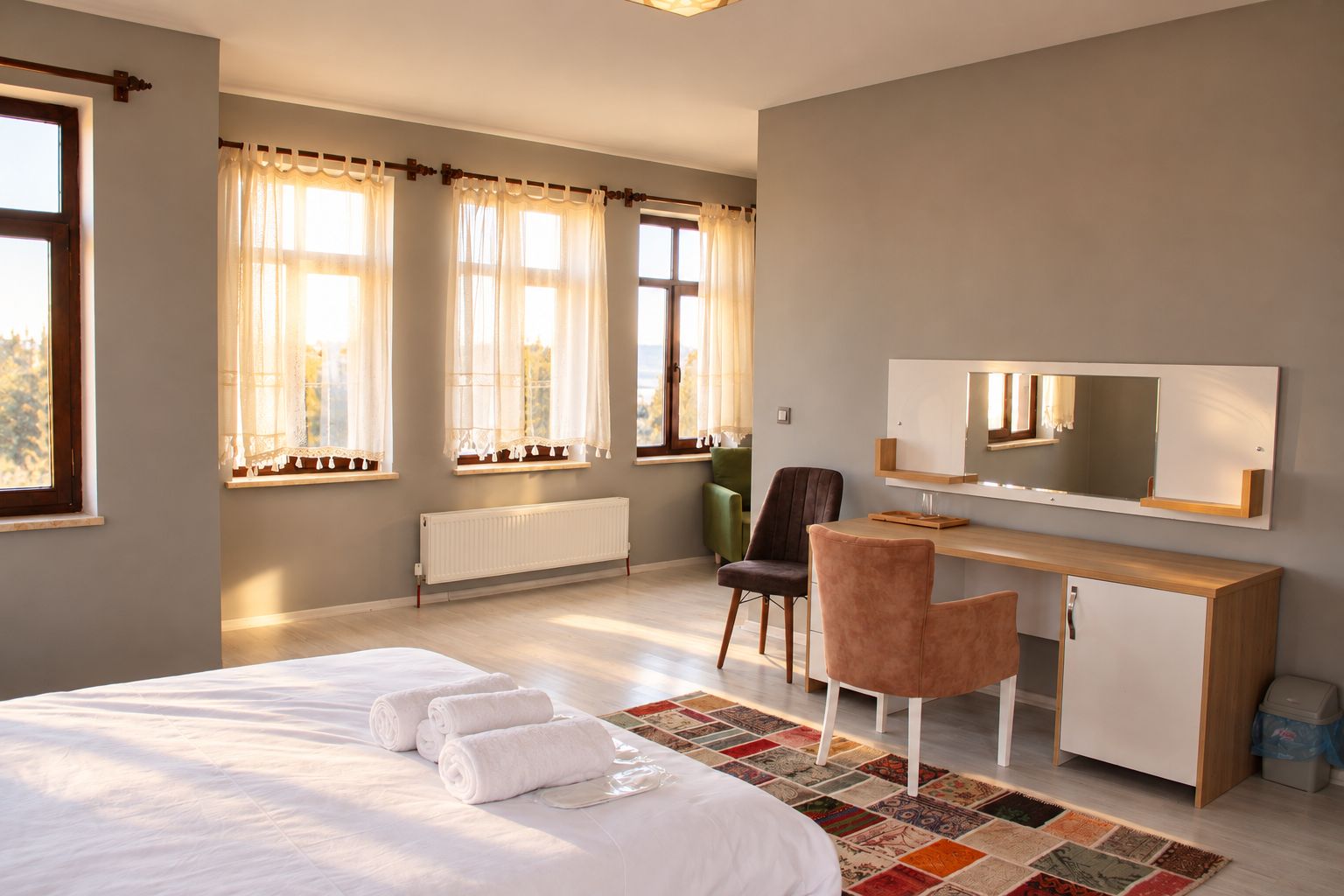 A hotel room with a bed, a desk, a chair, a radiator, and a window with curtains.