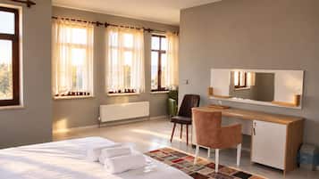 A hotel room with a bed, a desk, a chair, a radiator, and a window with curtains.
