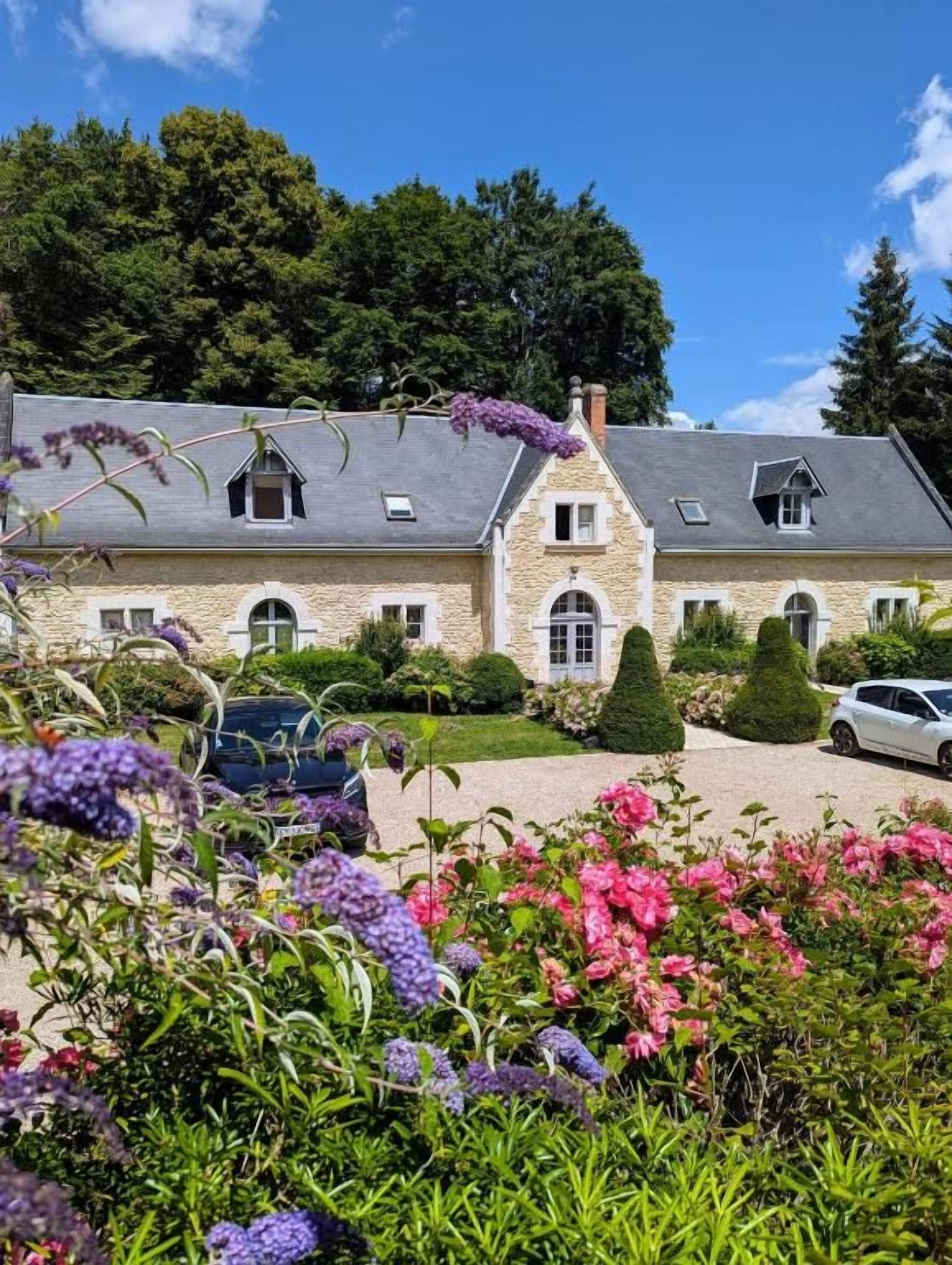 A stone building with a symmetrical facade, a central entrance, and a driveway leading to a parked car.