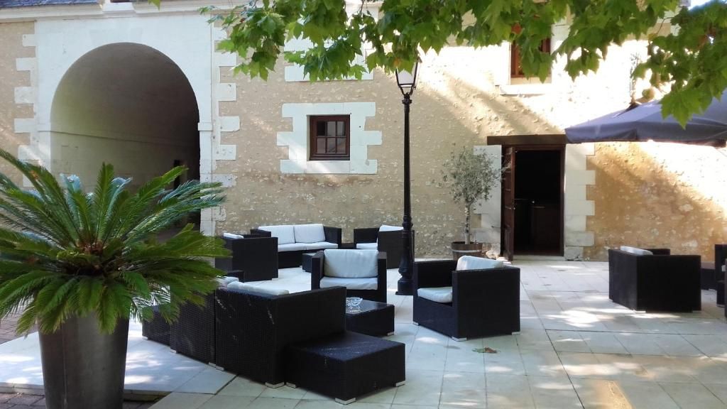Un espacio al aire libre con sofás y mesas, una planta en maceta, y un edificio con un arco y un ventanal.