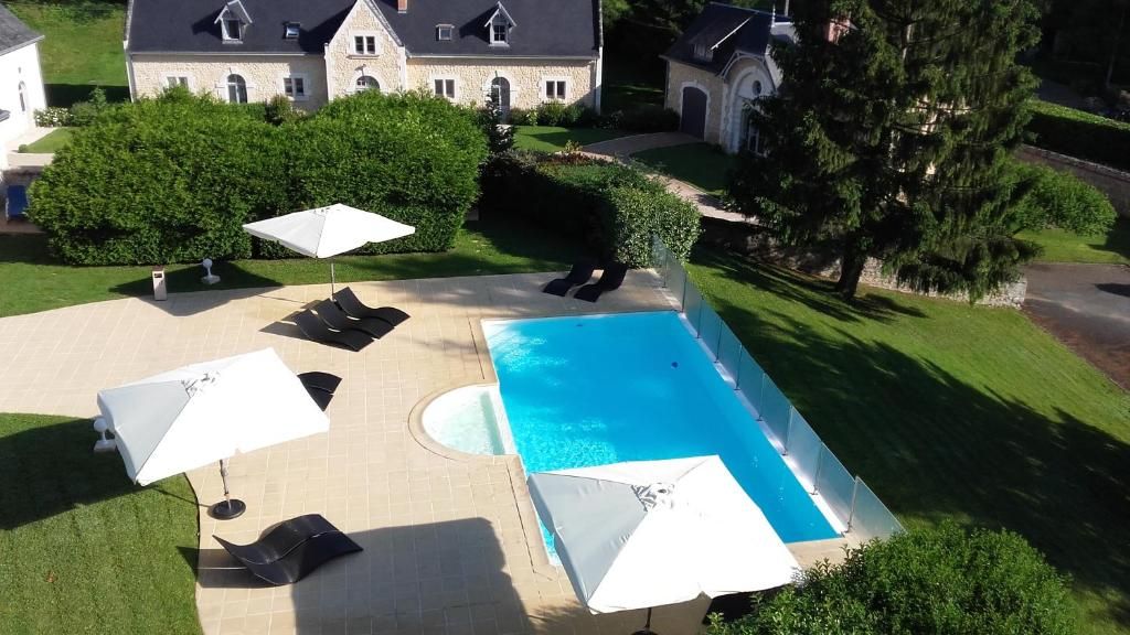 Piscina com espreguiçadeiras e guarda-sóis, rodeada por um gramado bem cuidado e uma casa grande ao fundo.
