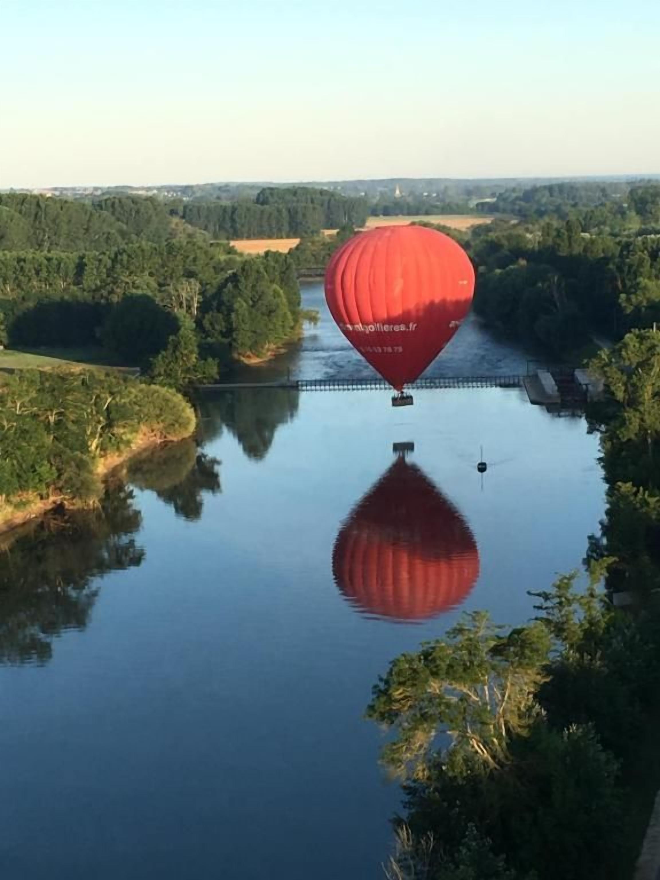 Een luchtballon boven een rustige rivier met een brug op de achtergrond.