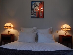 Un dormitorio con una cama, dos lámparas de noche, un cuadro en la pared y una mesita de noche.
