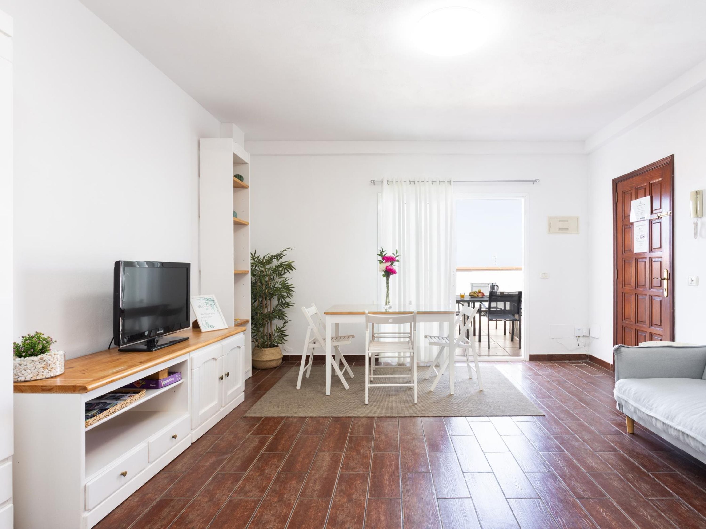 A modern living room with a flat-screen TV, a dining table with chairs, a sofa, and a potted plant.