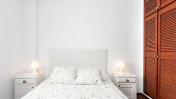 A bedroom with a bed, two bedside tables with lamps, and a wooden wardrobe.