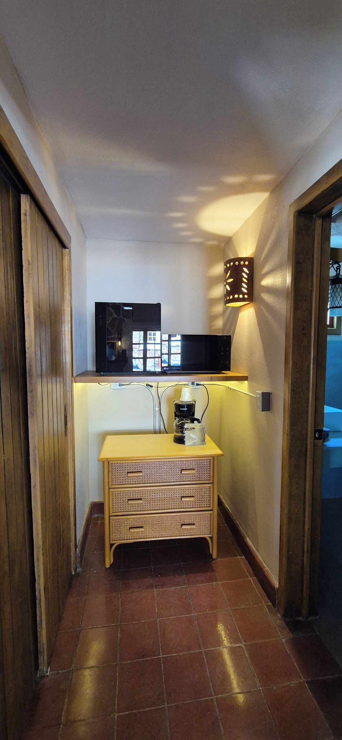 Een smalle gang met een houten kast, een koffieapparaat en een wandlamp.