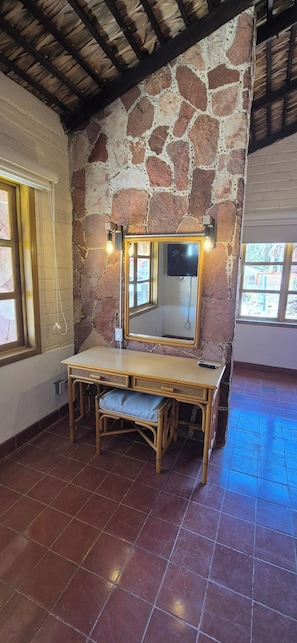 A room with a stone wall, a wooden vanity with a mirror, a bench, and tiled flooring. - Sandy Shores 8A y 8B (La Paz)