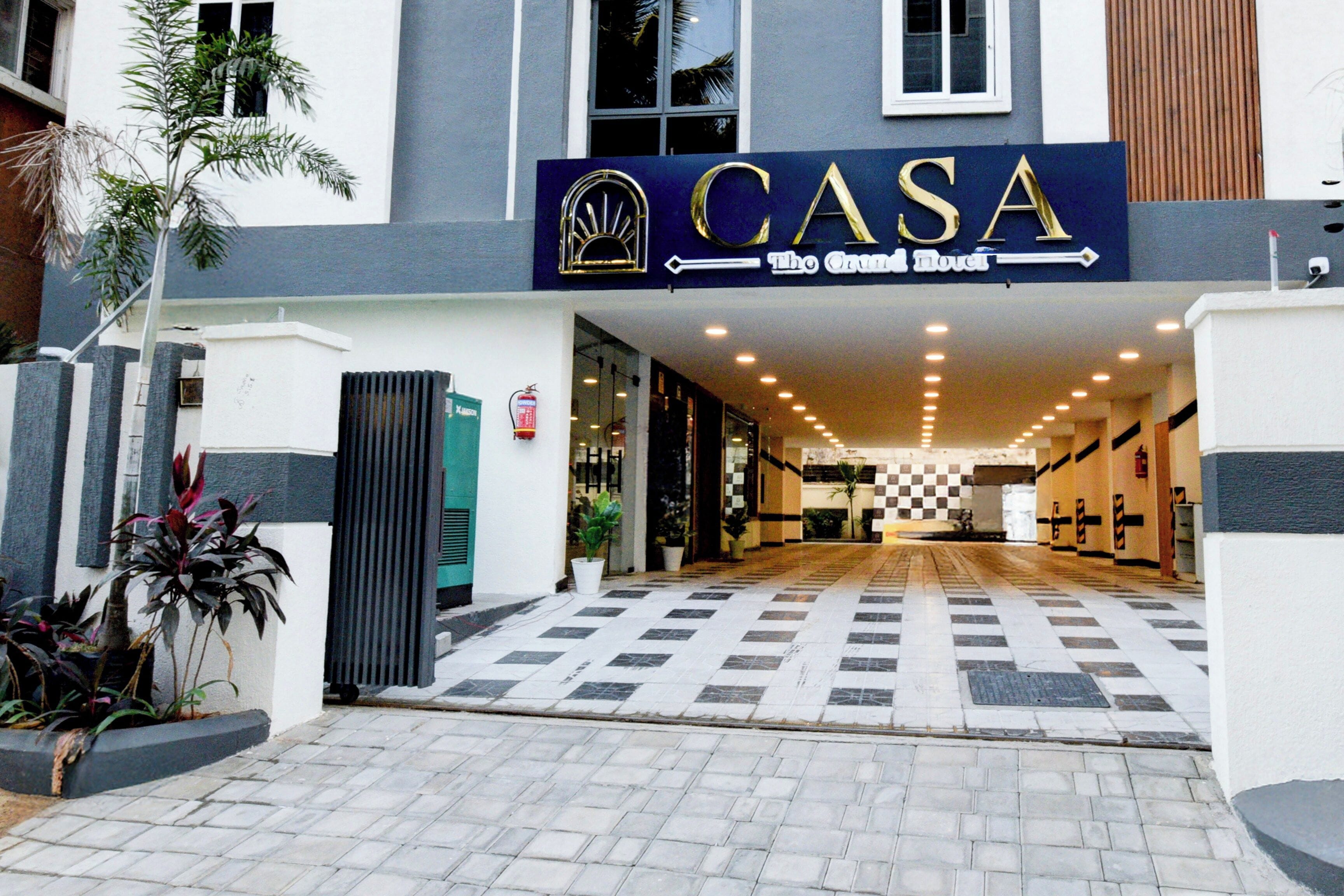 Entrada de un hotel con piso a cuadros, un letrero que dice 'CASA The Grand Novel' y una cámara de seguridad sobre la entrada.