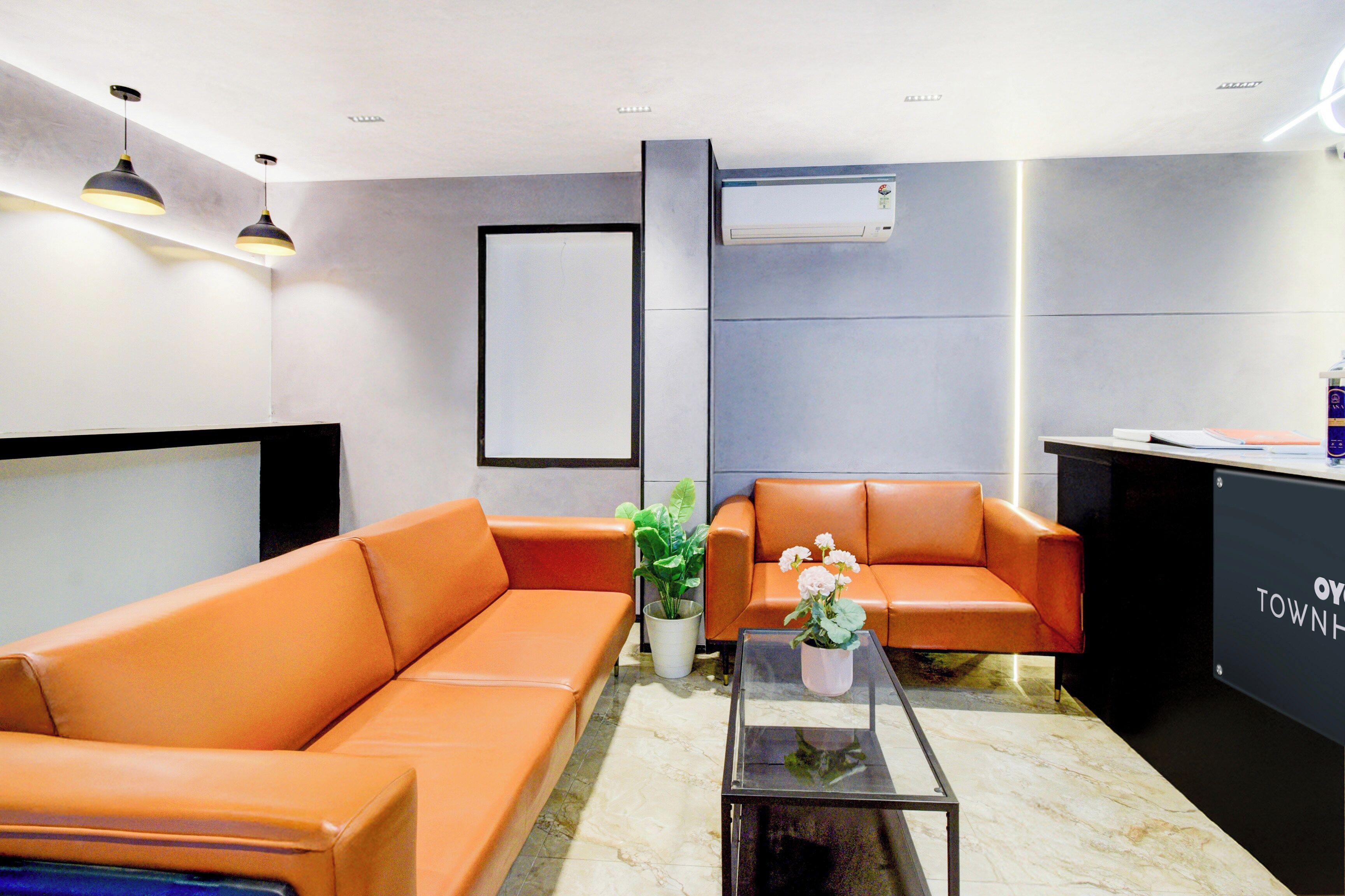 A modern waiting area with orange sofas, a glass coffee table, and a reception desk.