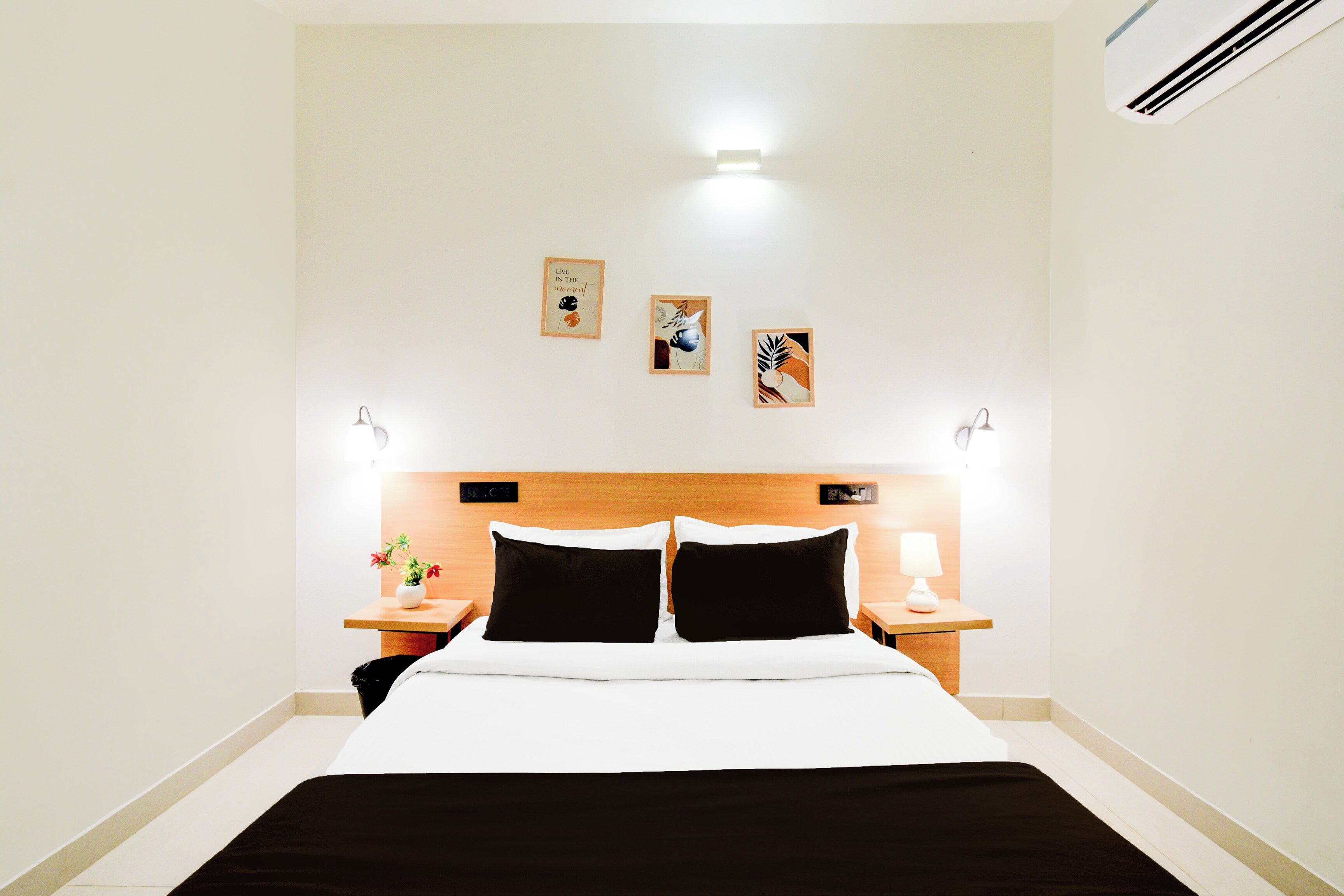 A hotel room with a bed, two bedside tables, a nightstand, and three wall-mounted artworks.