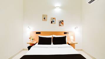 A hotel room with a bed, two bedside tables, a nightstand, and three wall-mounted artworks.