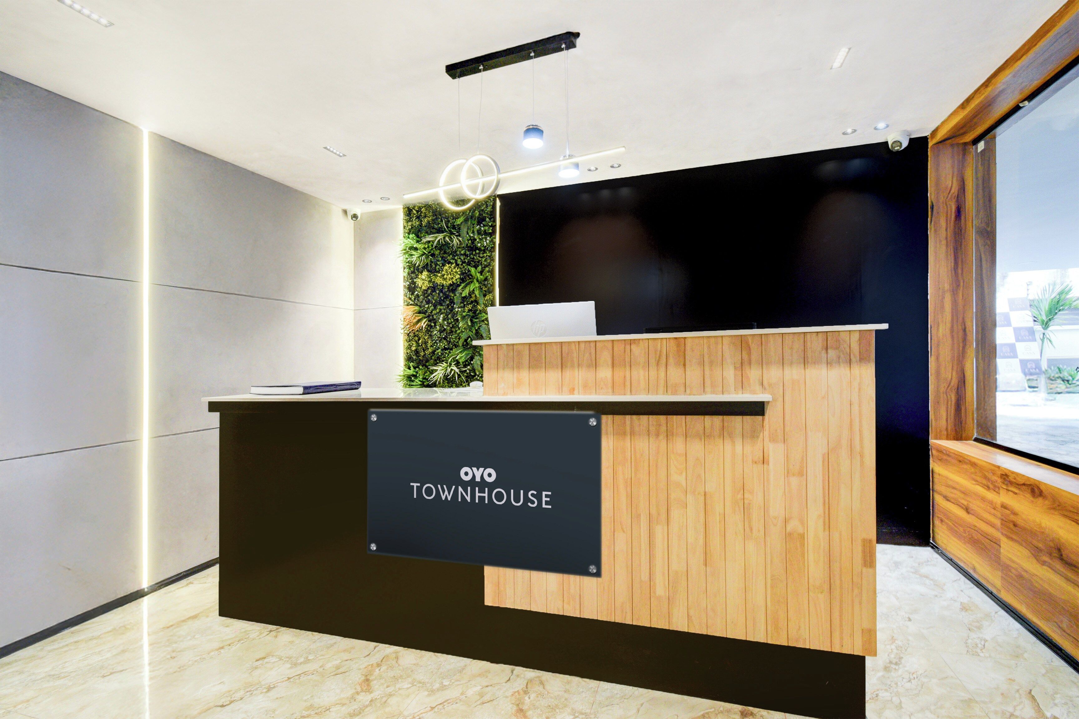 Un mostrador de recepción con un cartel que dice 'OYO TOWNHOUSE', un acabado de madera y una pared verde con plantas al fondo.