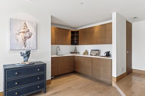 A modern kitchen with wooden cabinets, a sink, and a countertop. There is a decorative sculpture on a dresser and a framed artwork on the wall. - Mountain & City Views | Hot Tub + Sauna | Trails to Mt Sanitas | Castle Black (Boulder)