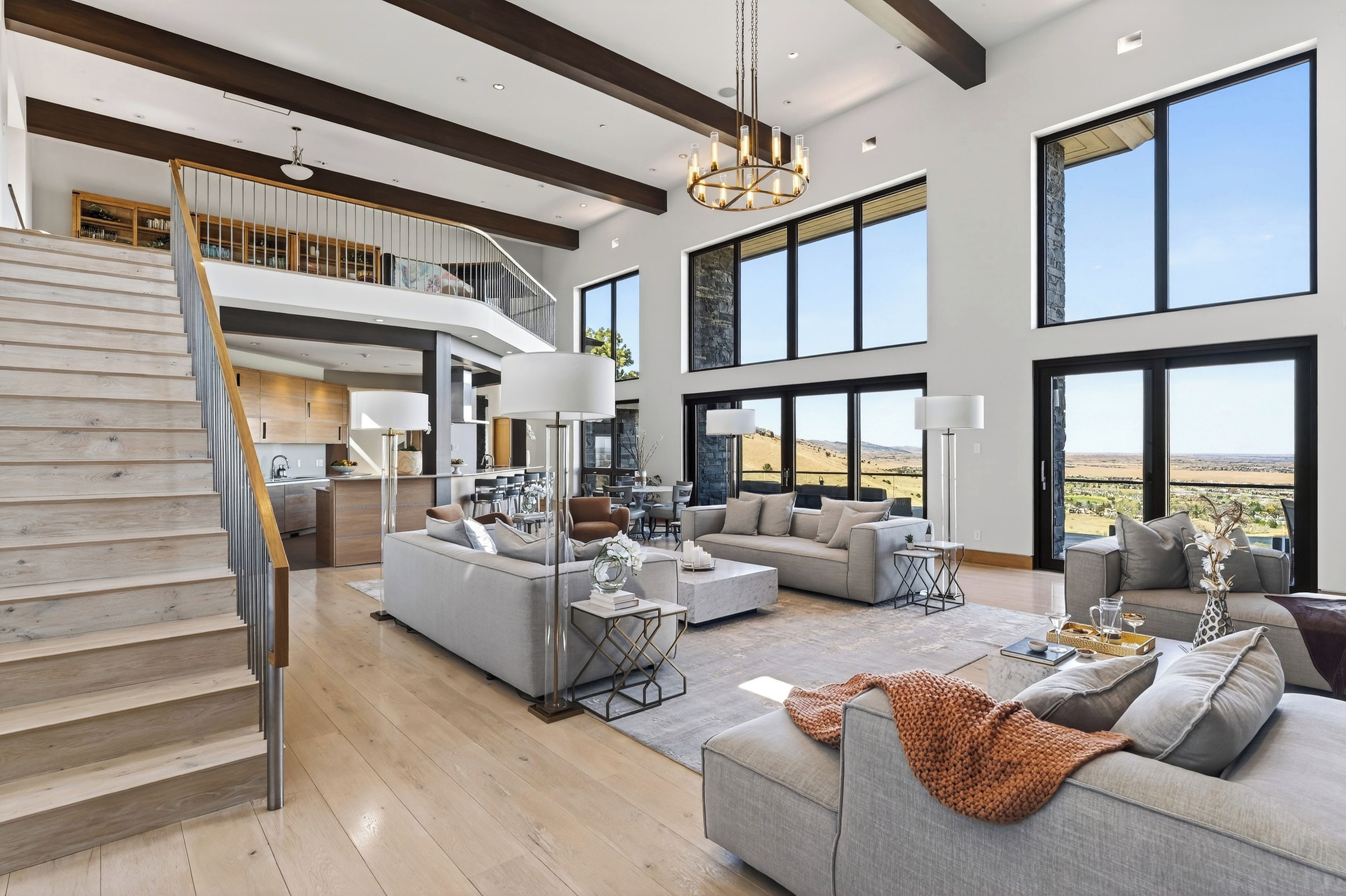 A spacious living area with a staircase, large windows, and a view of the landscape.