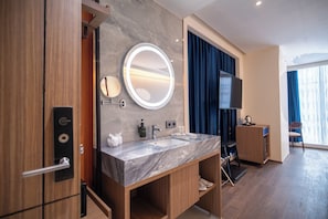 A modern hotel bathroom with a marble vanity, a round mirror, a television, and a treadmill. - ODST Jakarta Transit Hotel (Tangerang)