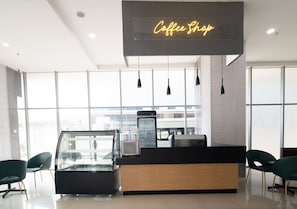 A modern coffee shop with a glass display case, a coffee machine, and a neon sign. - ODST Jakarta Transit Hotel (Tangerang)