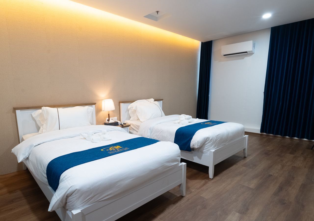 Habitación de hotel con dos camas, una mesita de noche, una lámpara, un equipo de aire acondicionado y una cortina.