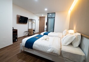 Ett hotellrum med två sängar, en tv som är monterad på väggen, ett träskåp och en spegel.