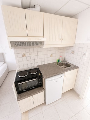 A compact kitchen with a built-in oven, a small refrigerator, and a sink. - Odysseus Apartments (Corfu)