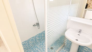 Un baño con cabina de ducha, lavamanos y baldosas estampadas.