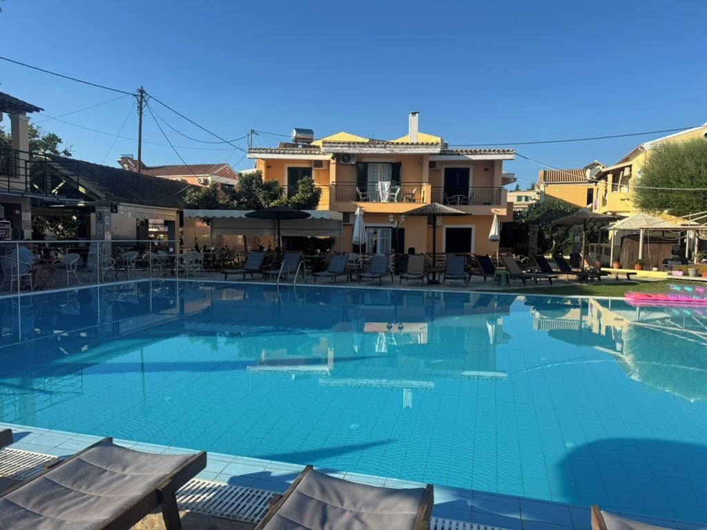 Una piscina con sillones de descanso, un edificio con balcones y un cielo azul despejado.