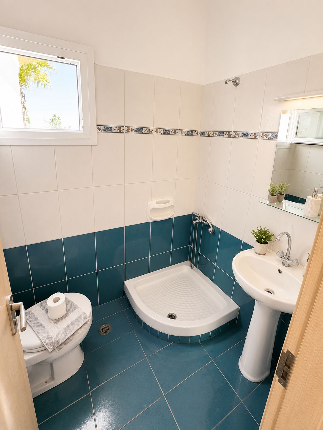 Bany amb vàter, bidet i rentapans, amb rajoles verda maragda i blanca, una finestra amb vista i una petita planta sobre el rentapans.