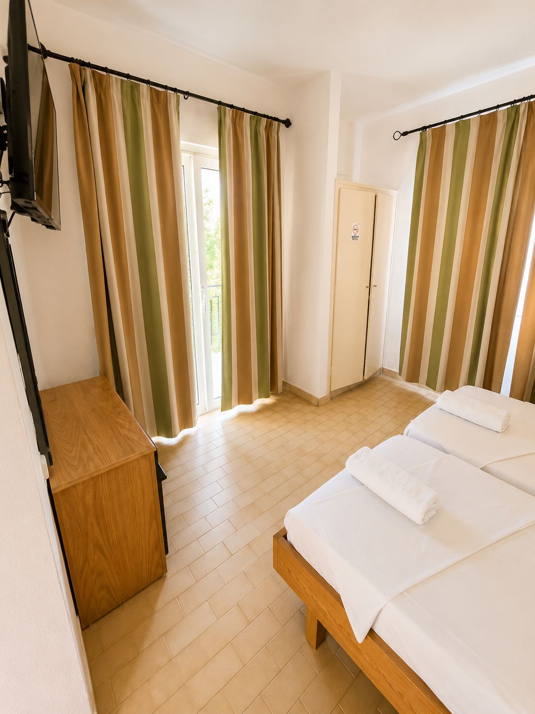 A hotel room with a bed, a wooden desk, a wardrobe, and curtains.