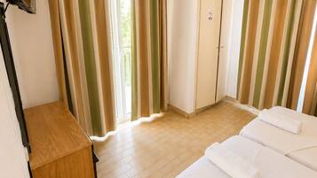 A hotel room with a bed, a wooden desk, a wardrobe, and curtains.