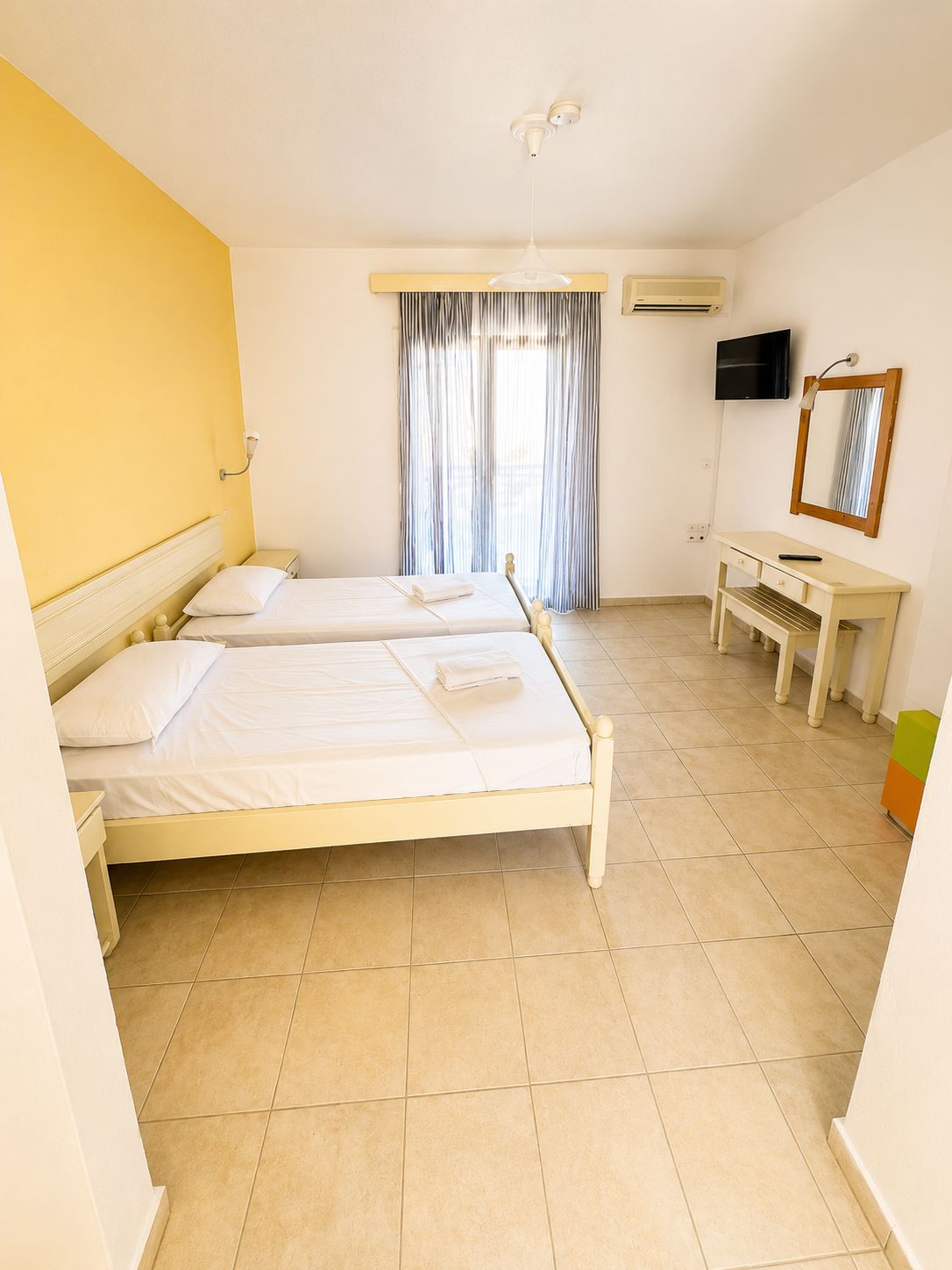 Habitación de hotel con dos camas, televisor, espejo y ventana con cortinas.