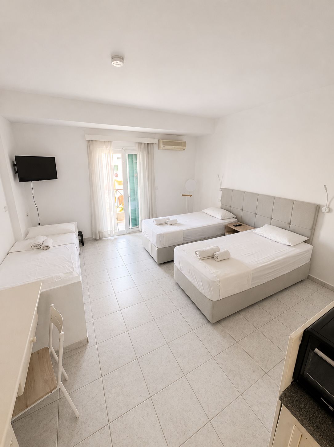 Habitación de hotel con dos camas, un escritorio, un televisor y una kitchenette.