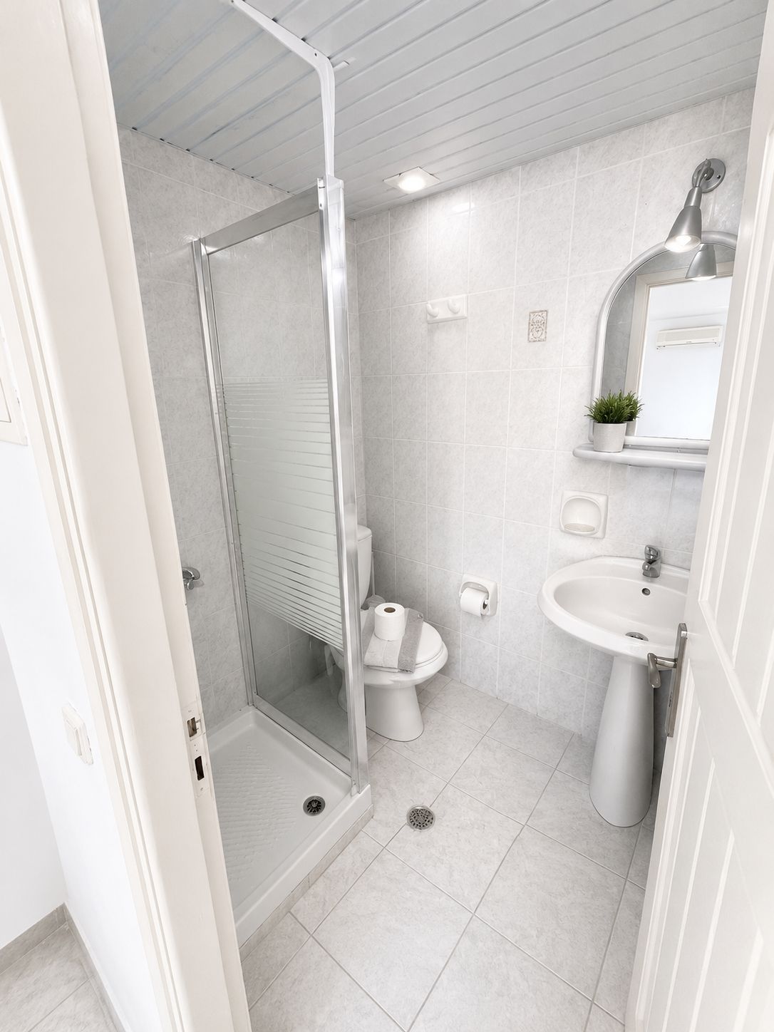 Un baño moderno con ducha de vidrio, inodoro, lavabo y espejo.
