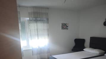 Ein Schlafzimmer mit einem Bett, einem Deckenventilator, einem Fenster mit Vorhängen und einem Wandbild.